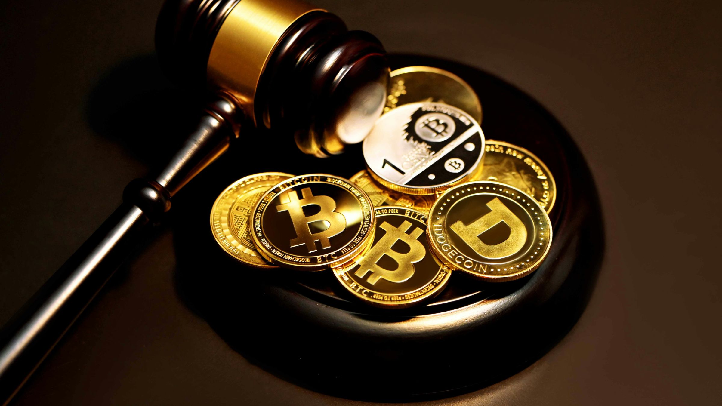 Judge’s gavel resting beside Bitcoin, Dogecoin, and other cryptocurrency tokens on a dark surface.