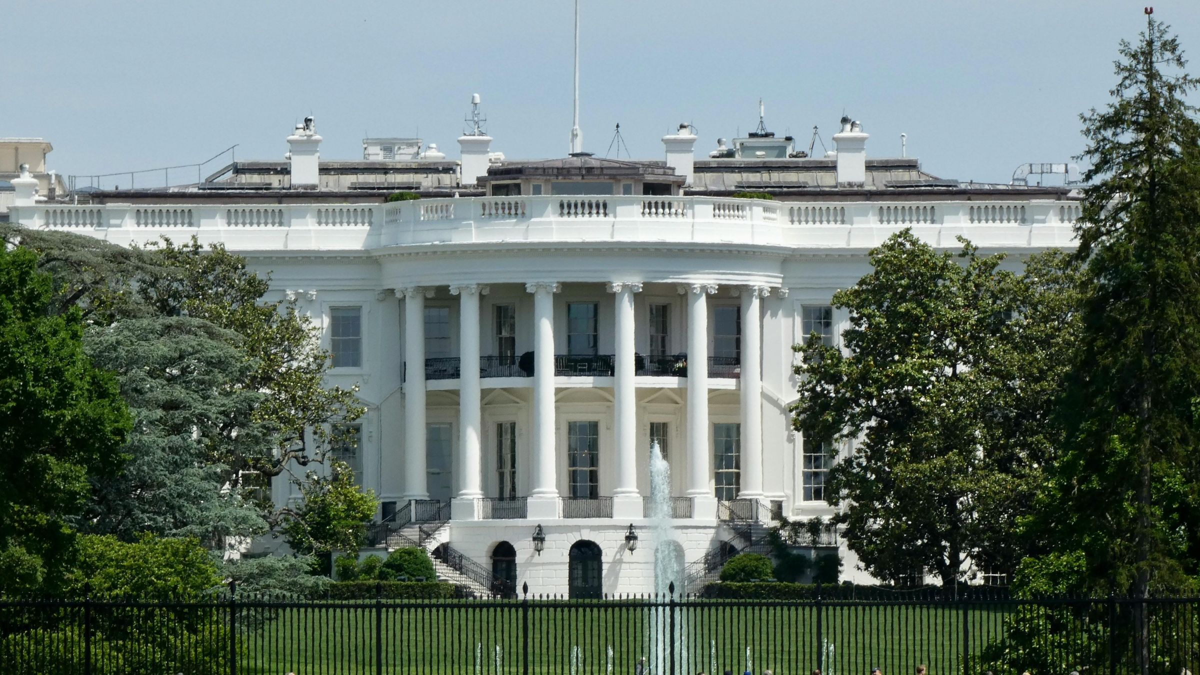 Rear view of the White House with columns, lawn, trees, and fountain in Washington.