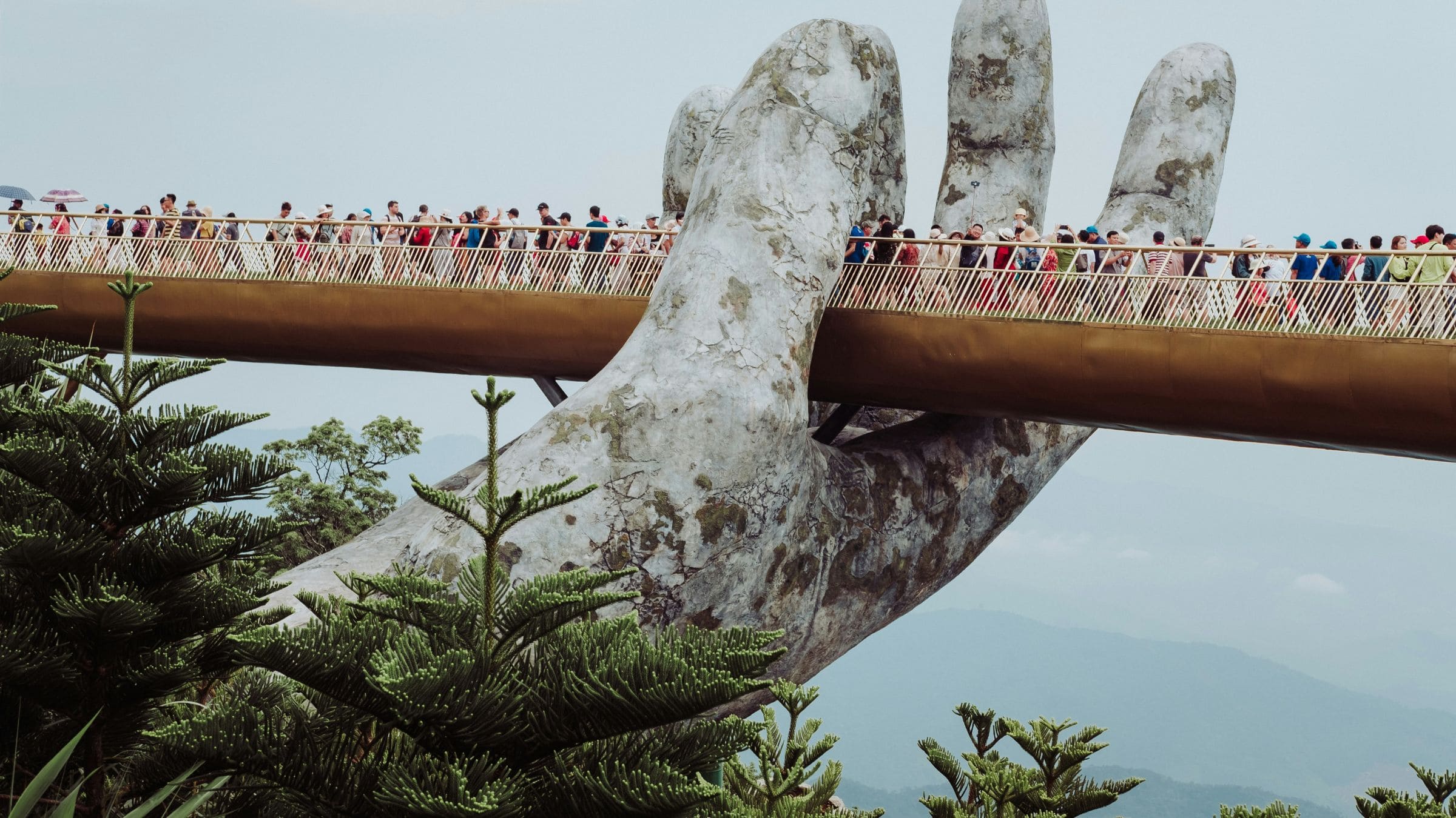 Crowds walk across the Golden Bridge in Da Nang, supported by giant stone hands above the hills.
