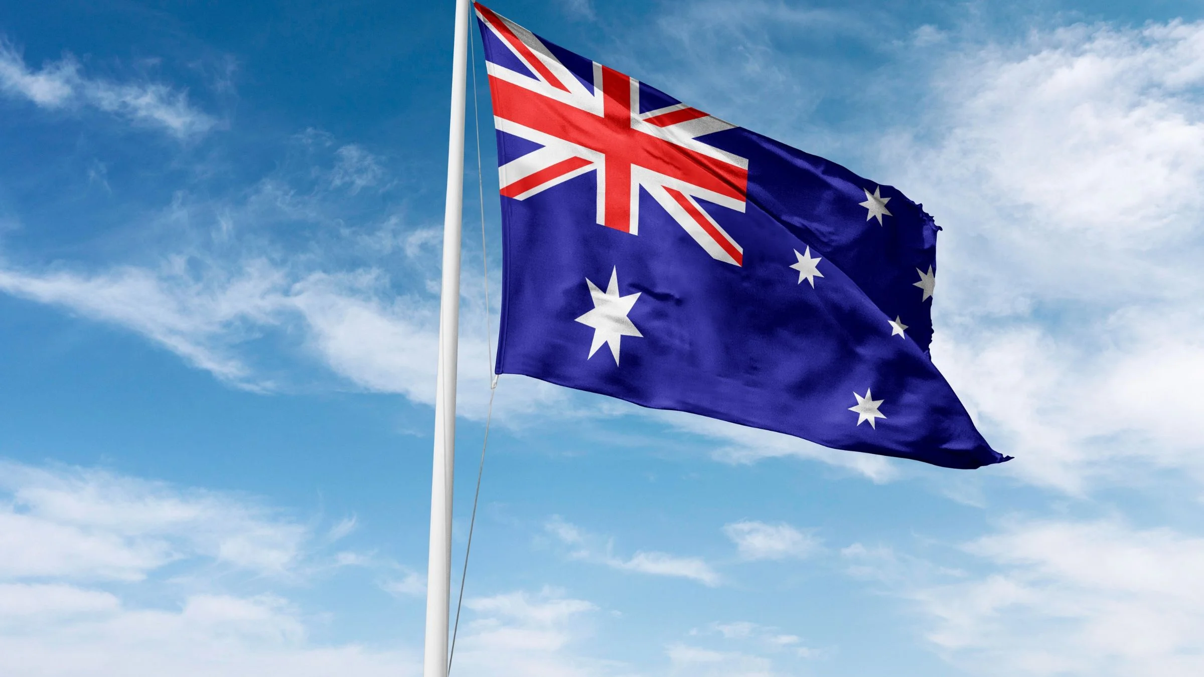 Australian flag flying on a flagpole against a blue sky with scattered white clouds.