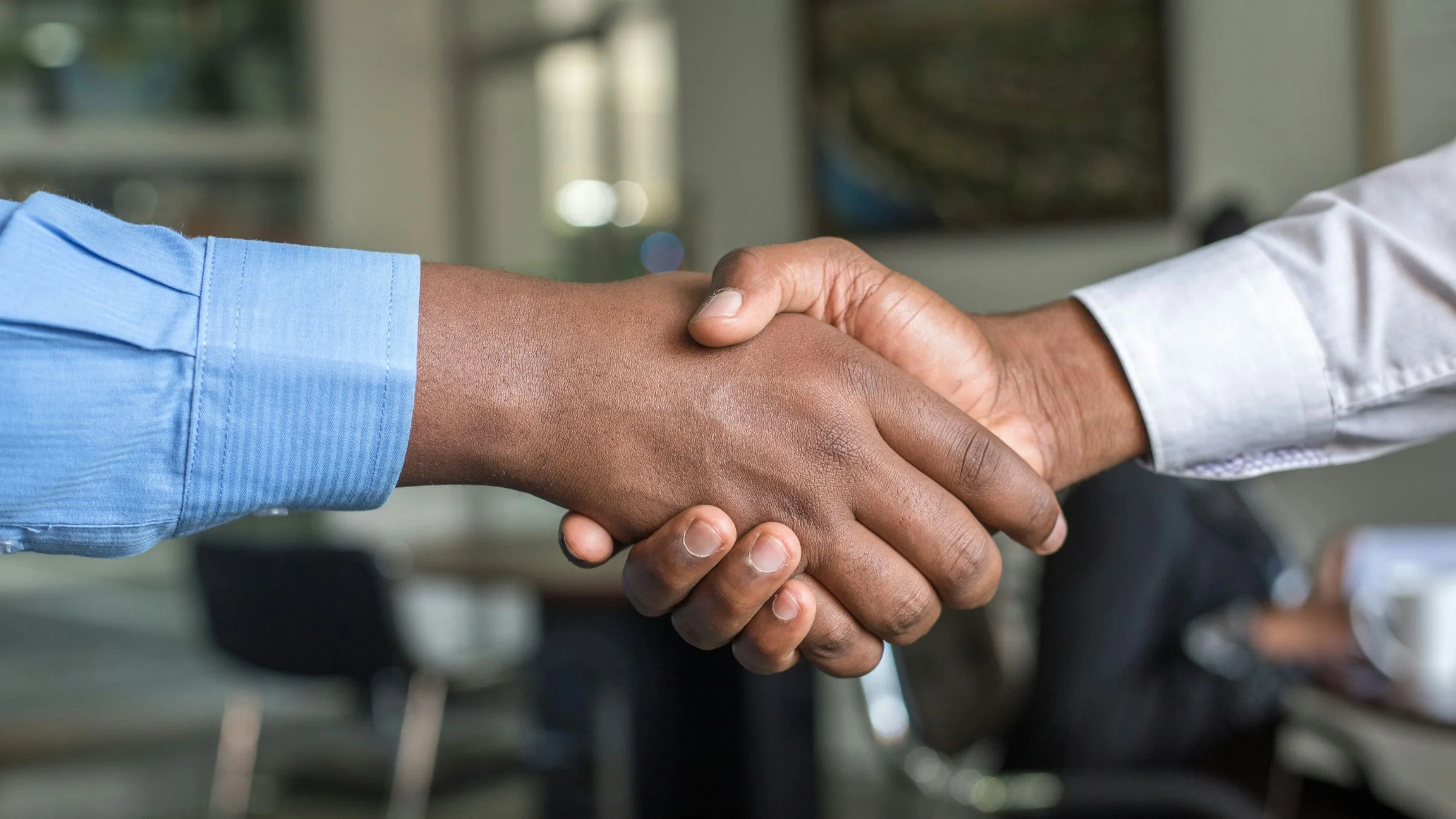 Close-up of two people shaking hands in an office setting during a business meeting.