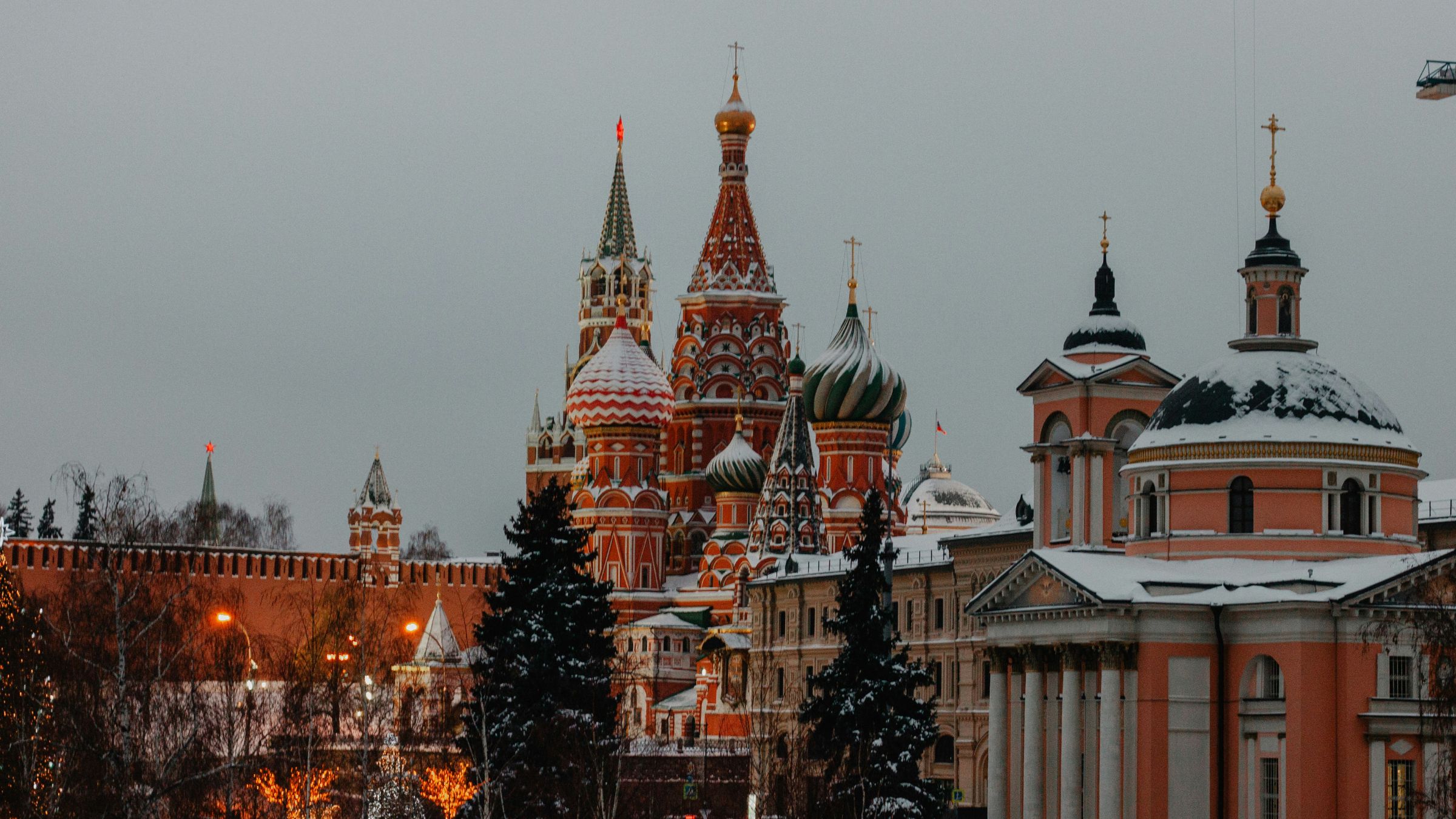 Snow-covered St. Basil’s Cathedral and Kremlin walls in Moscow seen under a gray winter sky.