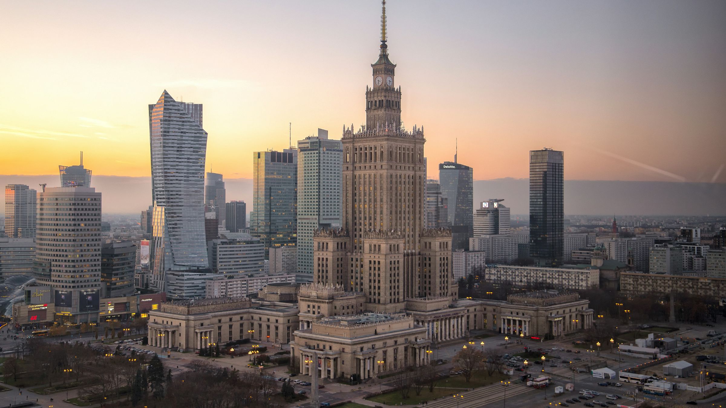 Warsaw skyline at sunset with the Palace of Culture and Science surrounded by modern high-rise buildings.