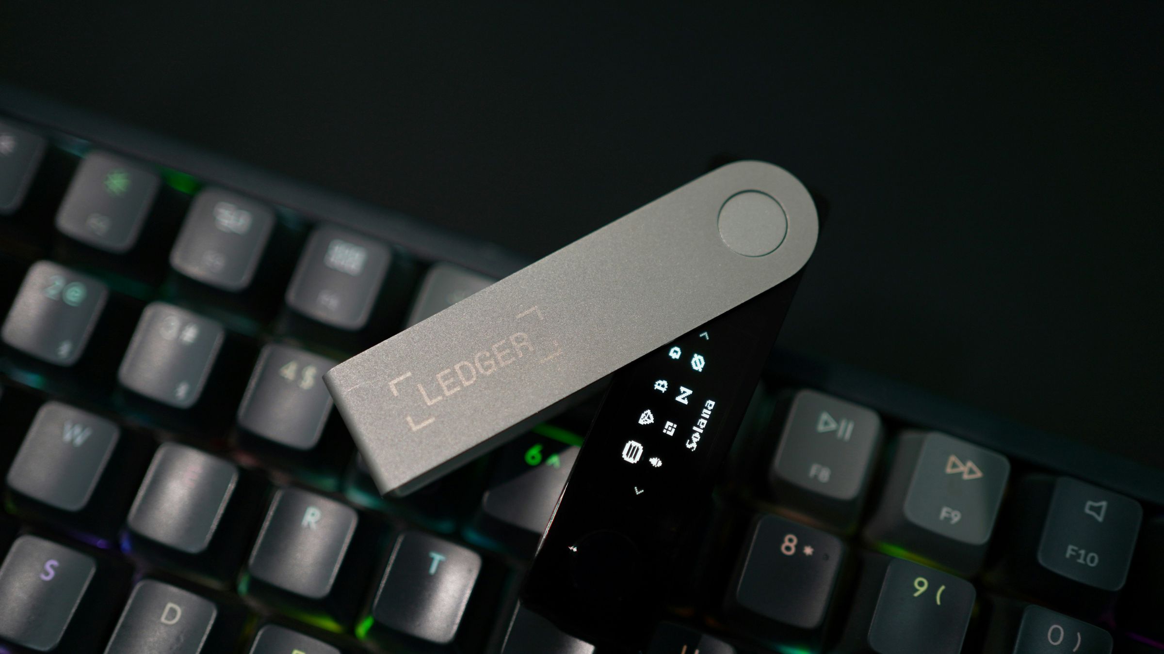 Ledger hardware wallet resting on a computer keyboard with its small display screen turned on.
