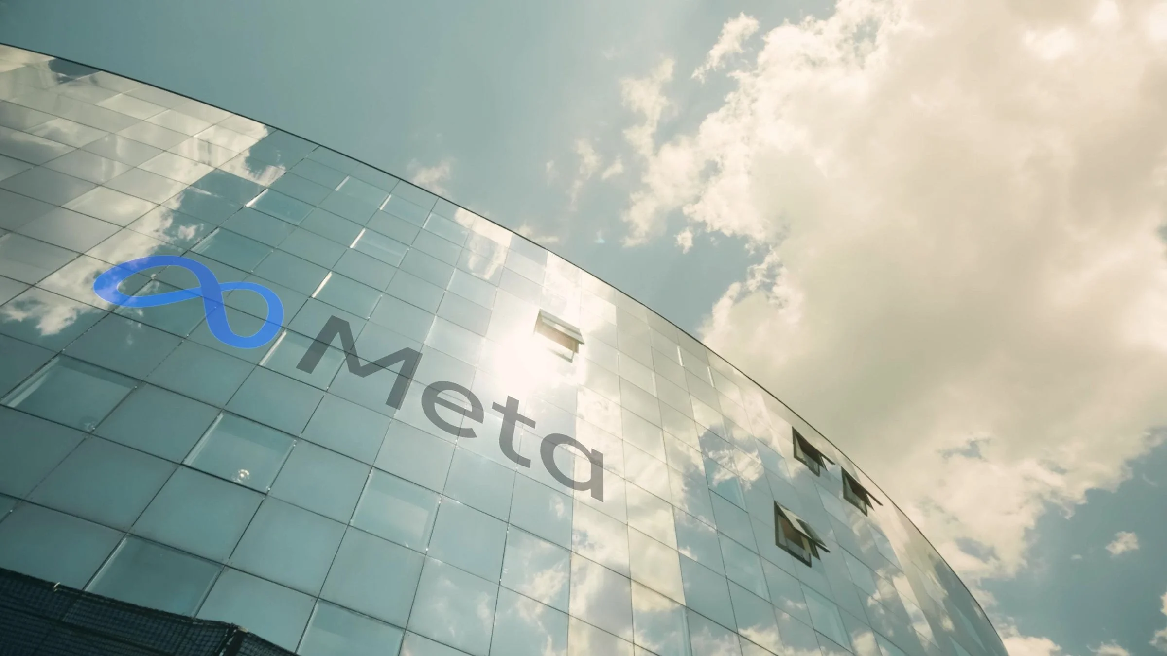Modern glass office building displaying the Meta company logo under a cloudy sky