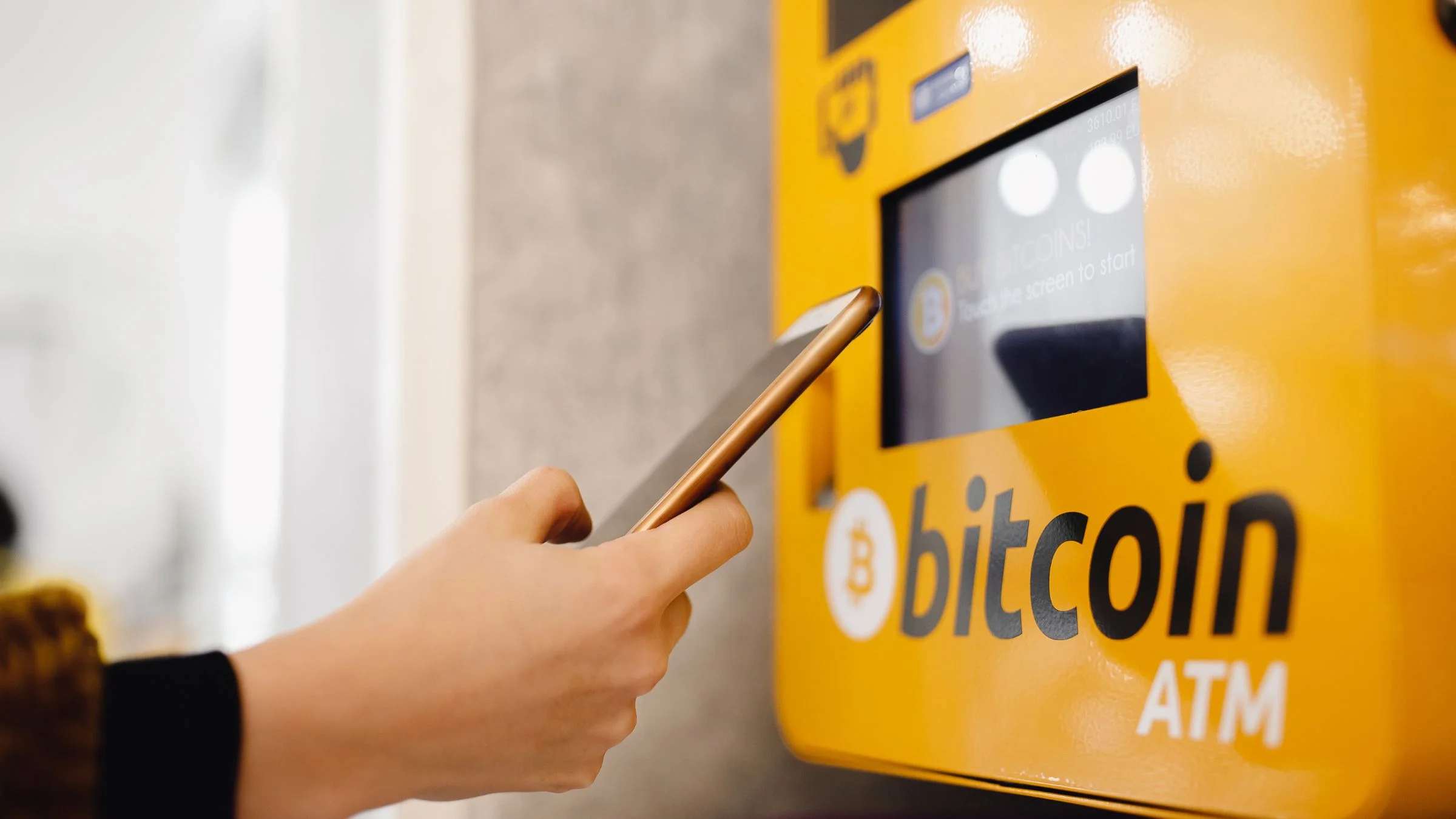 Close-up of a person using a smartphone near a Bitcoin ATM terminal