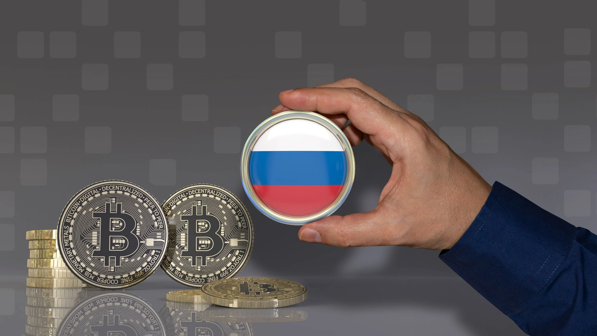 Hand holding a Russian flag medallion beside stacked Bitcoin coins on a gray background
