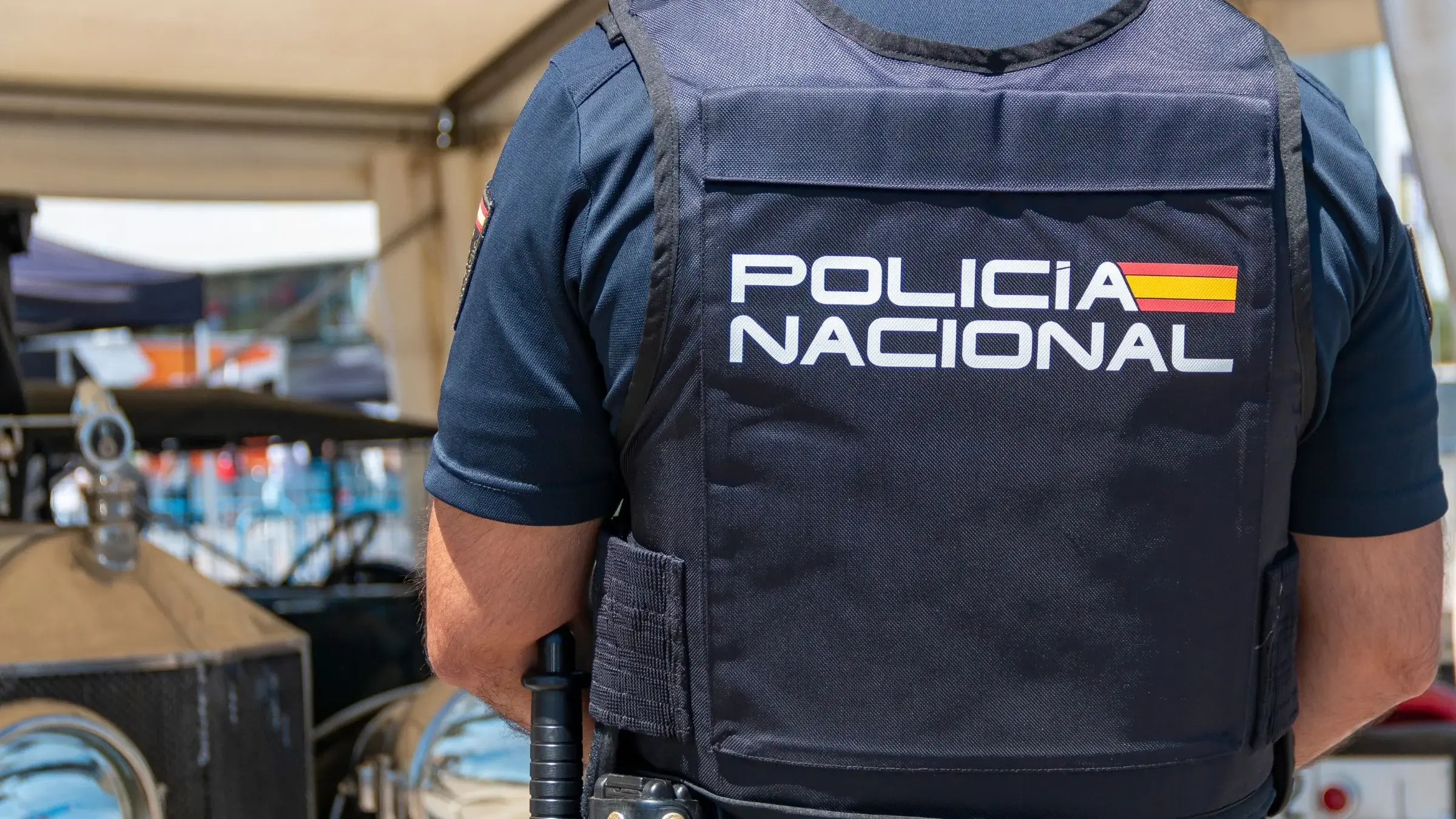 The back of a Spanish Policía Nacional officer wearing a dark tactical vest with the force's logo and Spanish flag insignia.