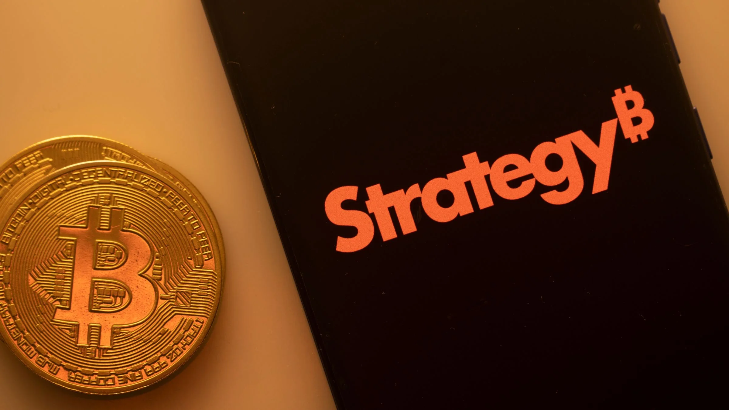 Physical Bitcoin coin beside a smartphone displaying the Strategy logo with a Bitcoin symbol