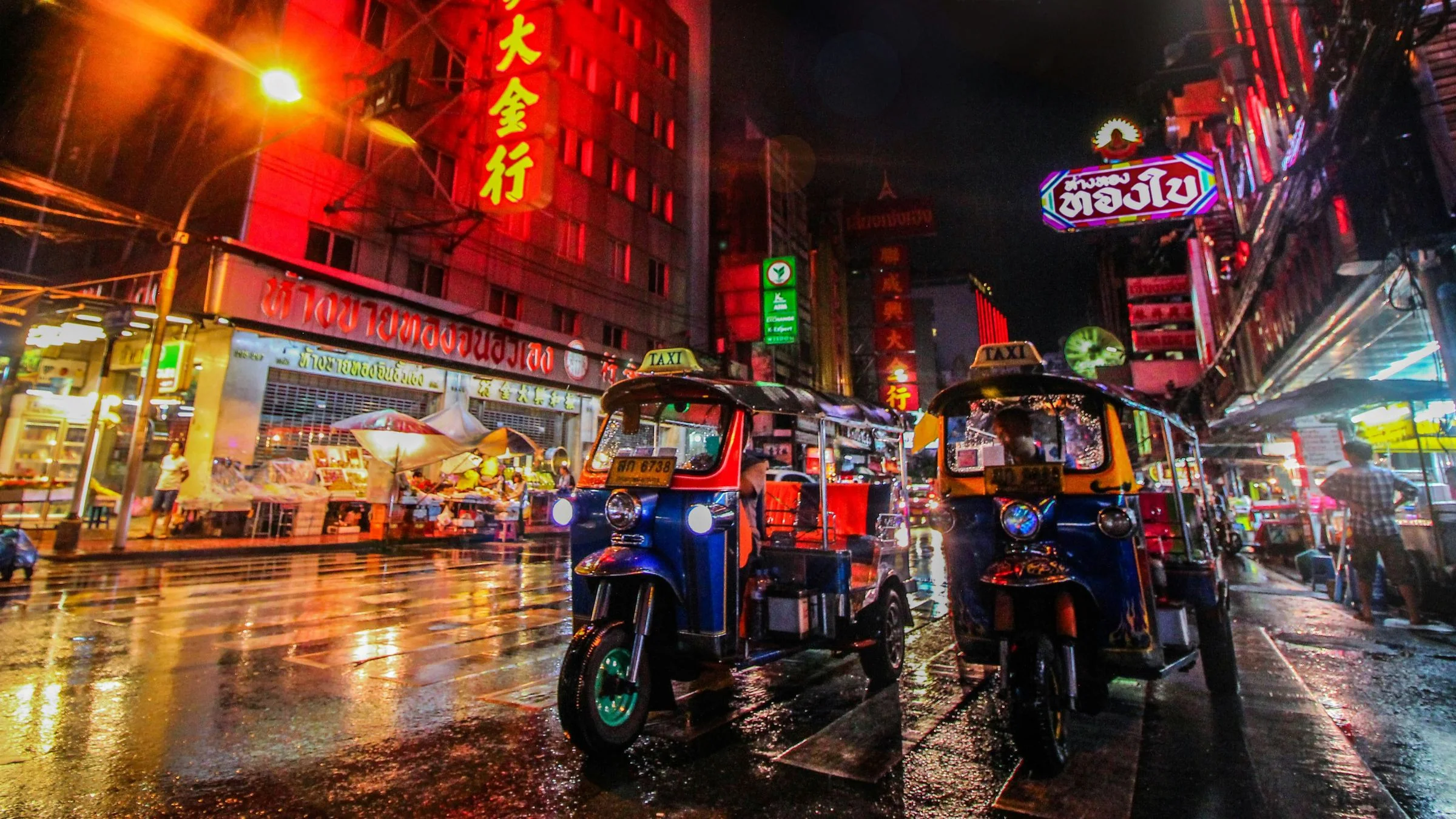 Tuk-tuks parked on a neon-lit street in Bangkok Chinatown at night after rain.