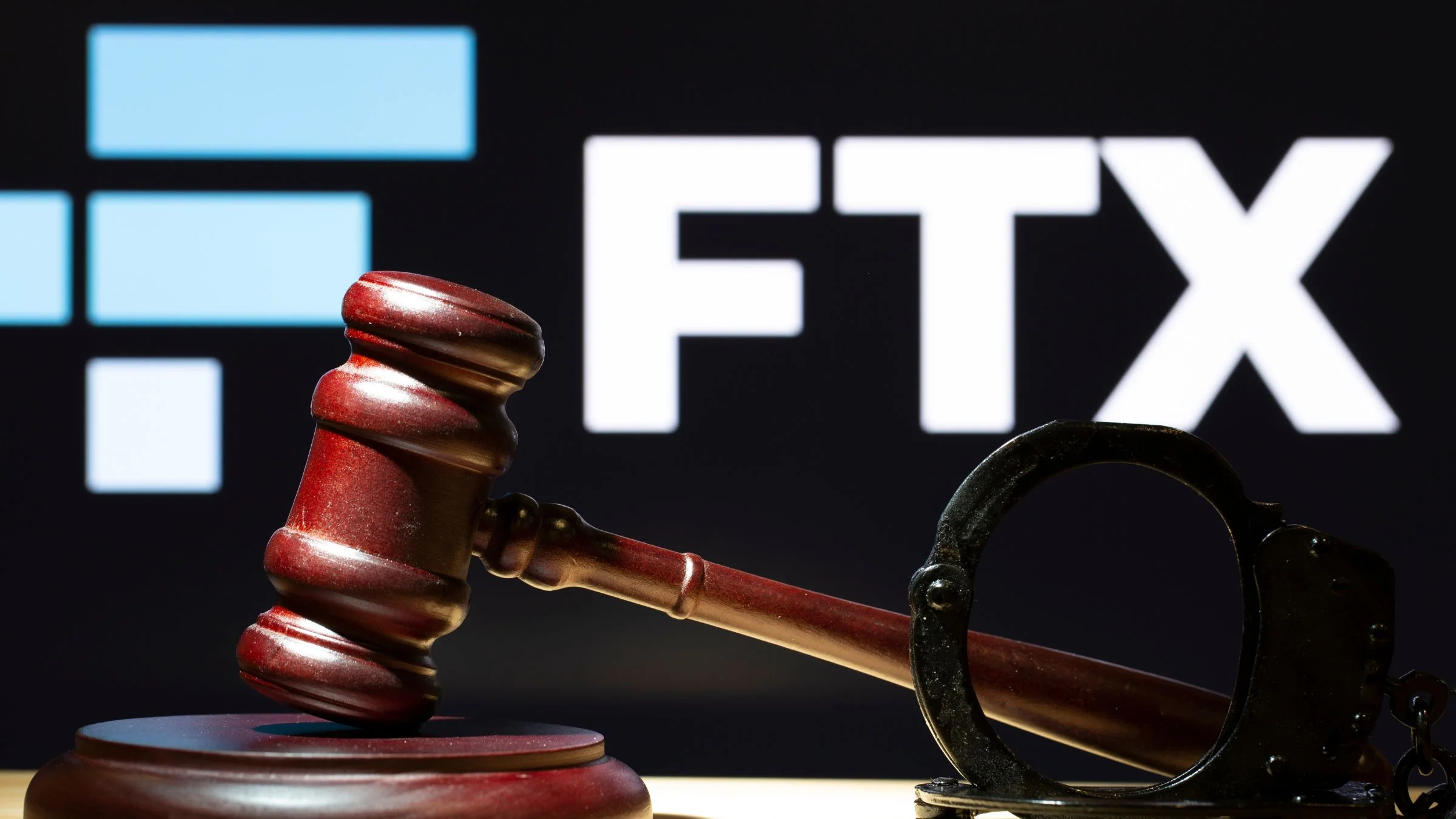 A judge's gavel and handcuffs in front of the FTX cryptocurrency exchange logo on a dark background