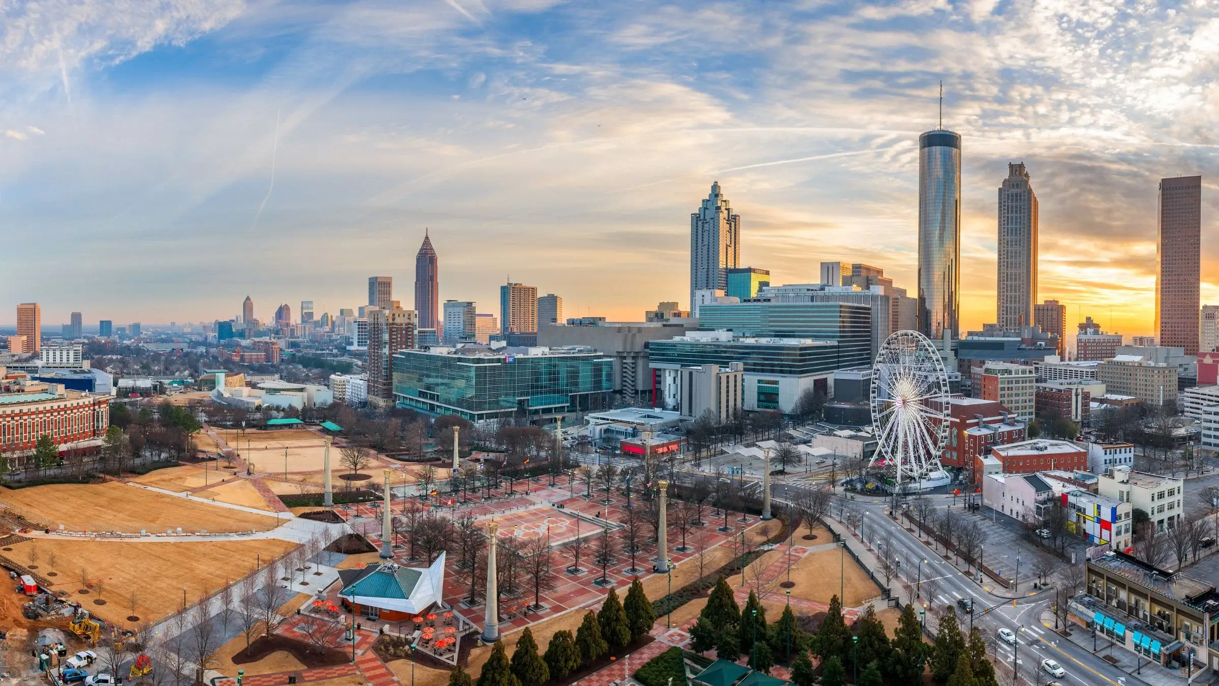 Panoramic view of downtown Atlanta skyline at sunset, with Centennial Olympic Park and a Ferris wheel below.
