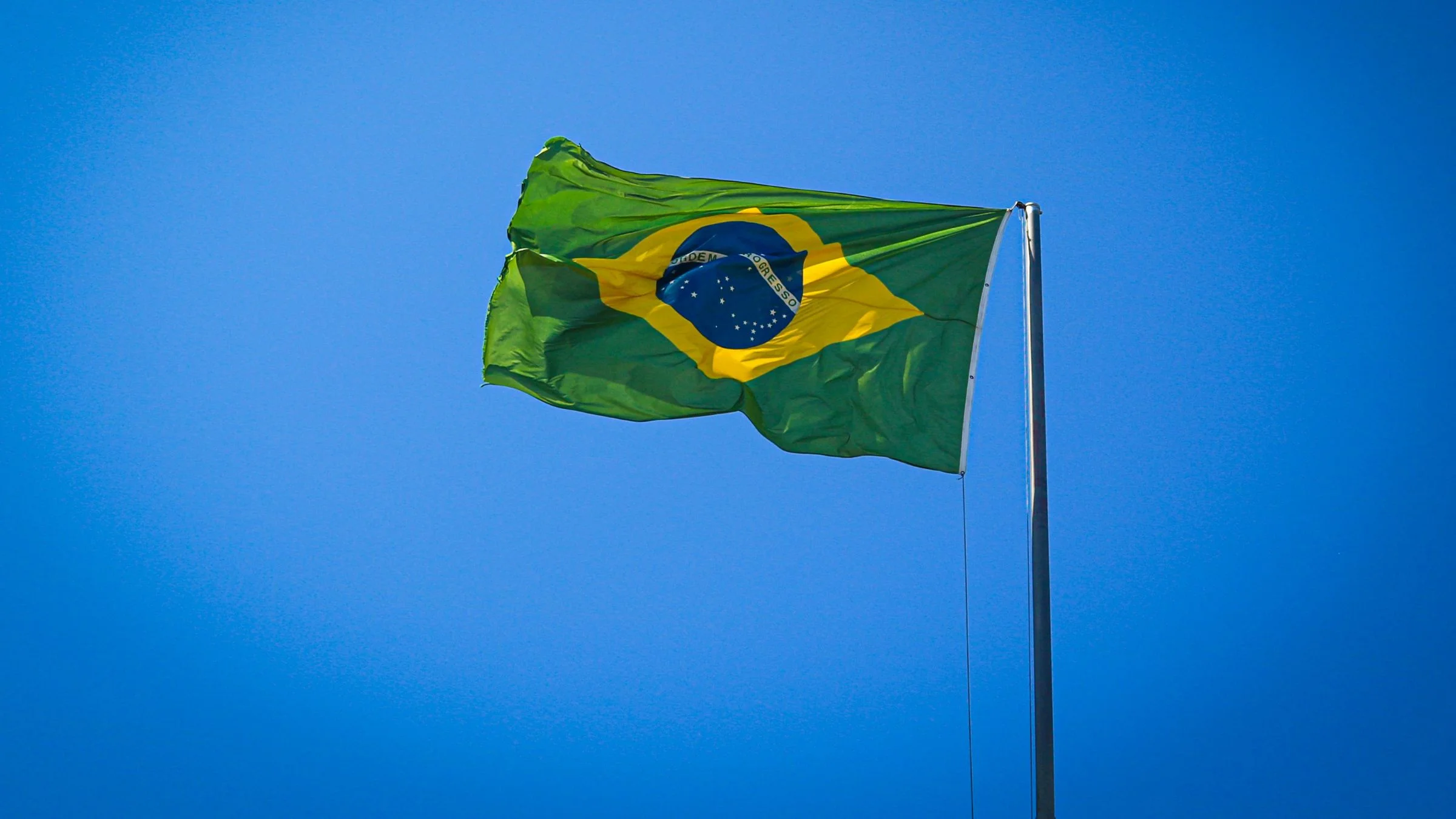 Brazilian flag flying on a flagpole against a clear blue sky.