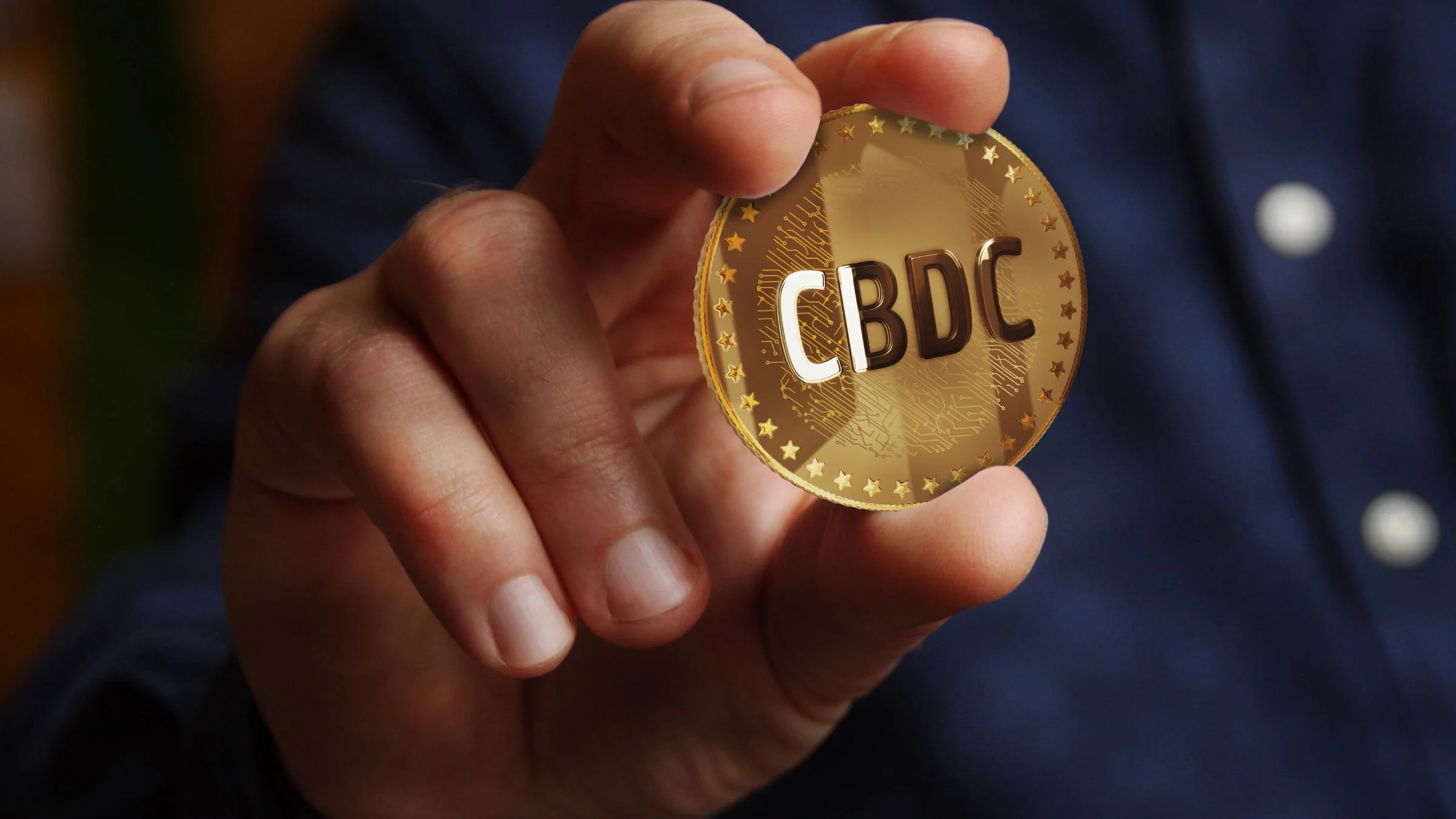 Hand holding a gold coin marked CBDC against a dark background, illustrating central bank digital currency.