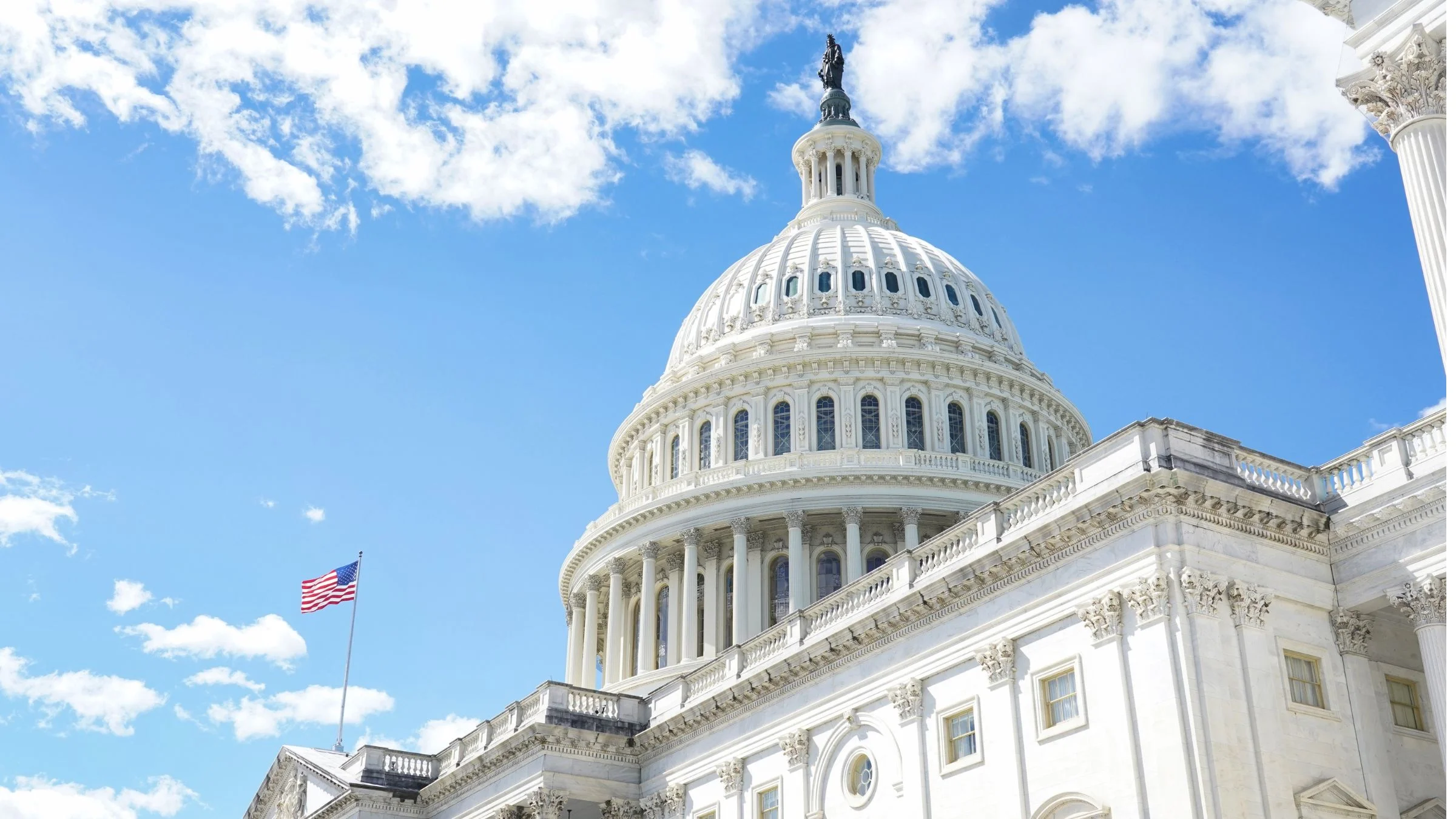 The U.S. Capitol Building dome against a blue sky with an American flag flying nearby