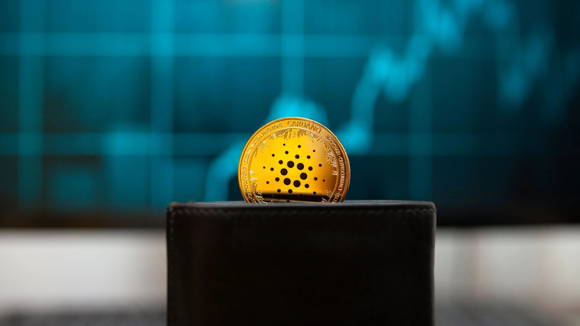 Gold Cardano token standing on a wallet with a blurred upward market chart in the background.