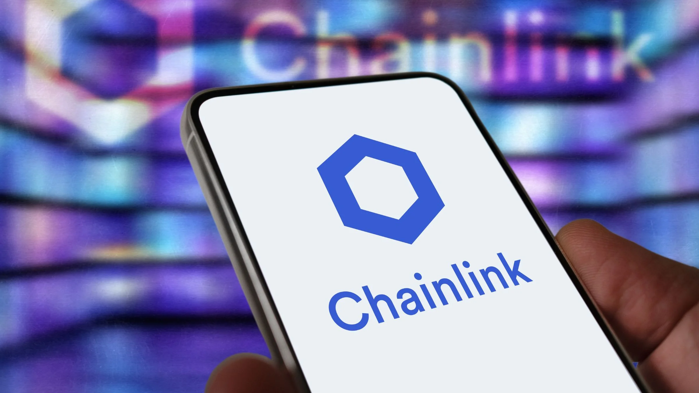 Hand holding a smartphone displaying the Chainlink logo with a blurred digital background behind it.