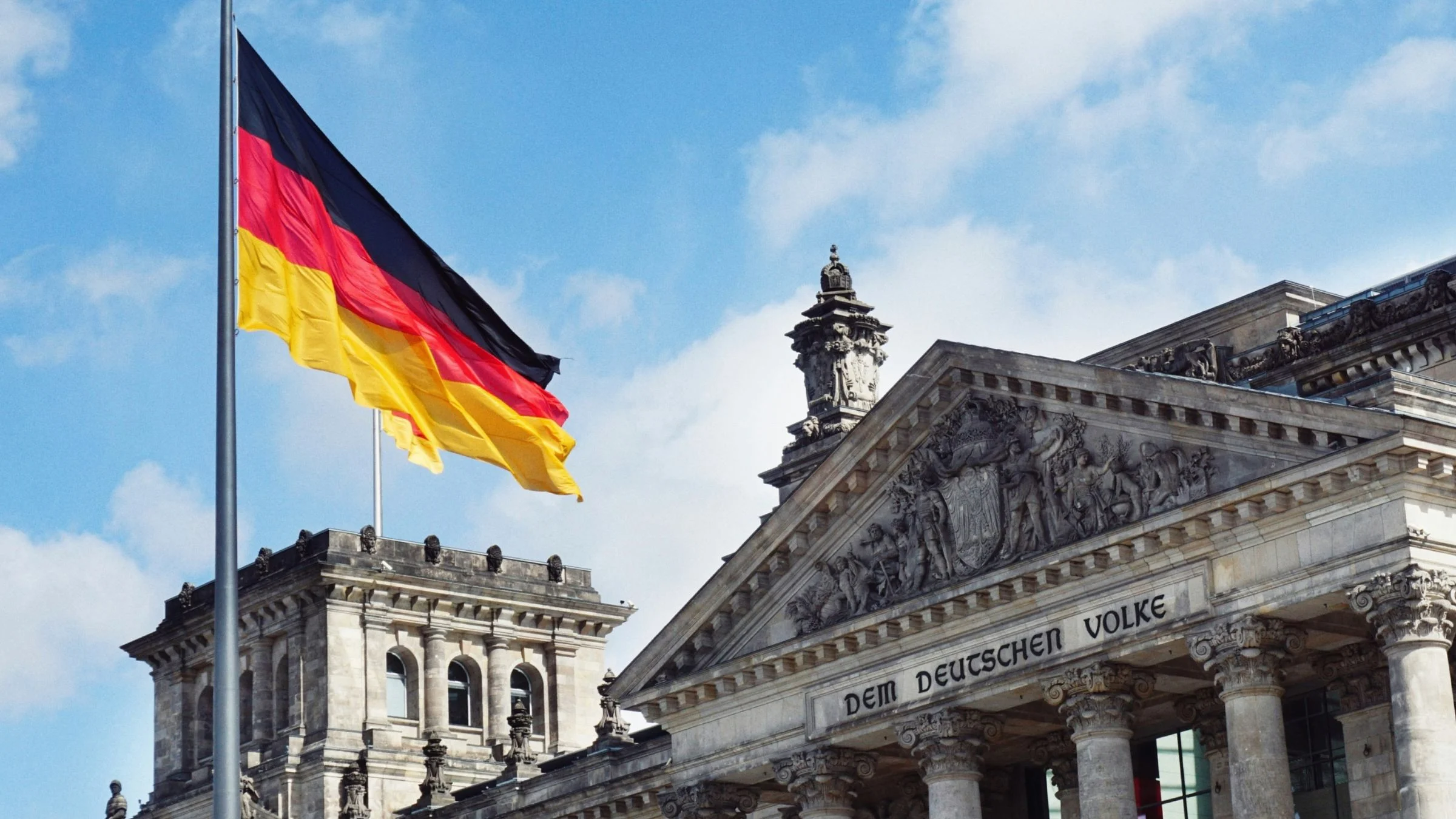 German flag flying beside the Reichstag building in Berlin under a bright blue sky.