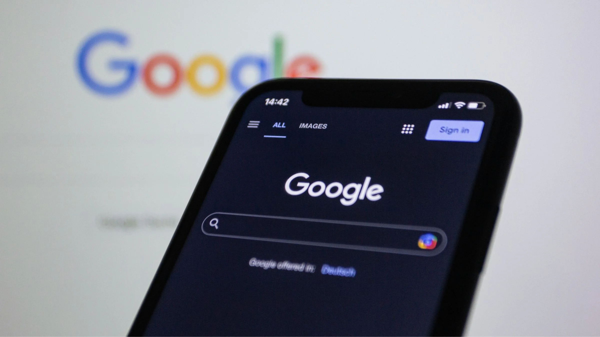 Smartphone displaying the Google search page in dark mode with a blurred Google logo in the background.