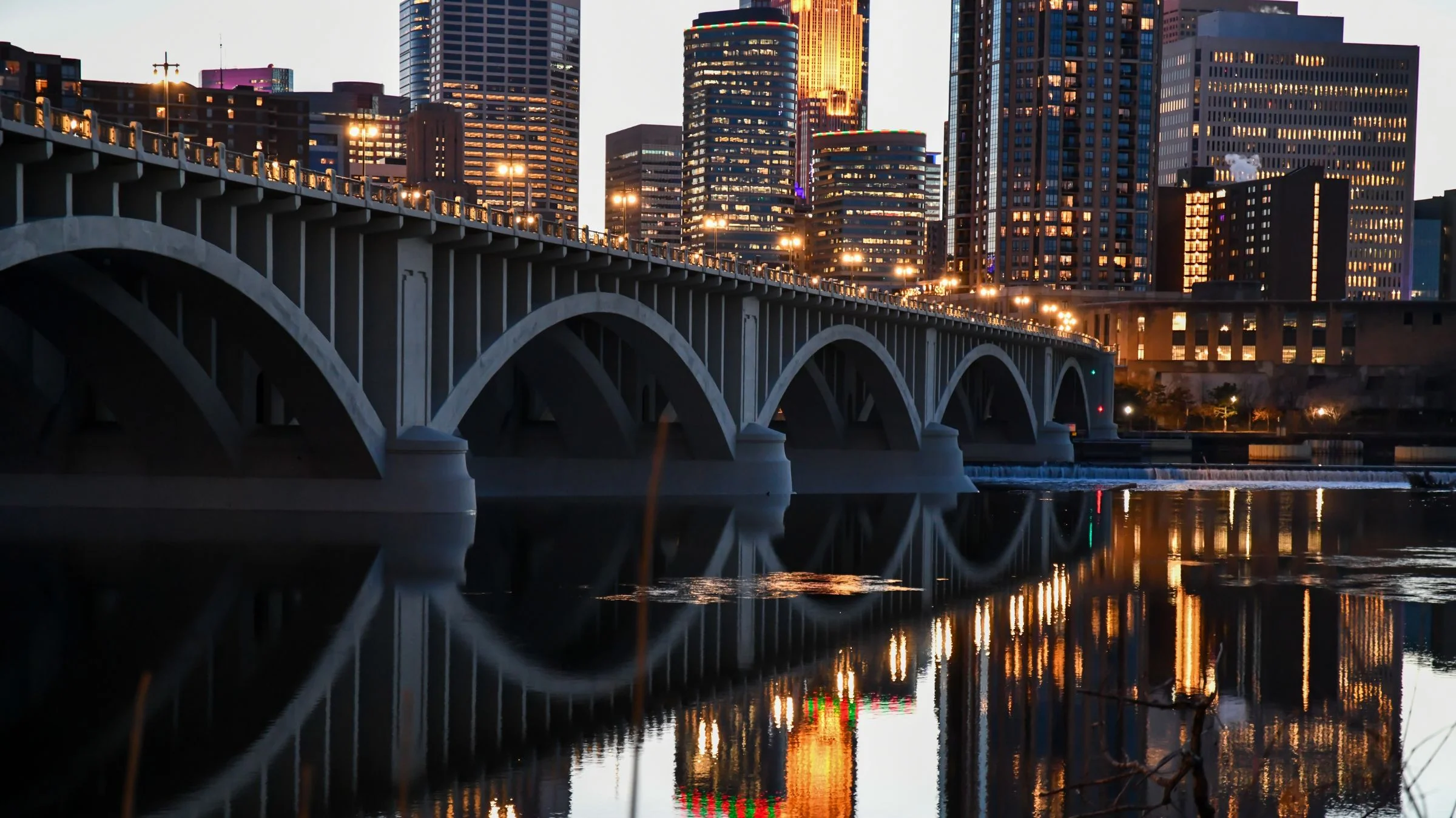 Arched bridge over the Mississippi River at dusk with the Minneapolis skyline in the background