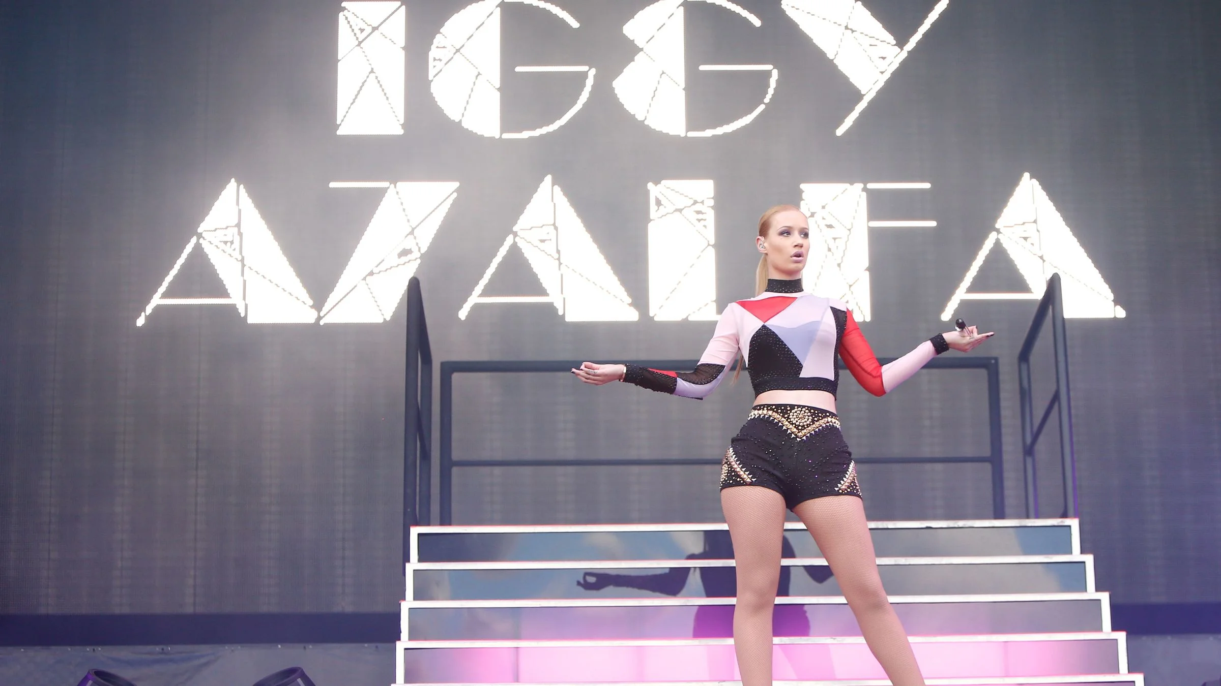 Performer on stage in front of large illuminated “IGGY AZALEA” text at a live show.