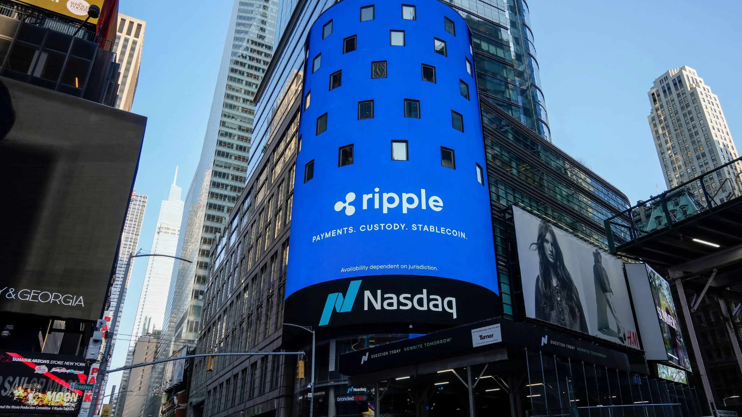 Large Ripple advertisement on a blue Nasdaq billboard mounted on a city building surrounded by high-rise towers.