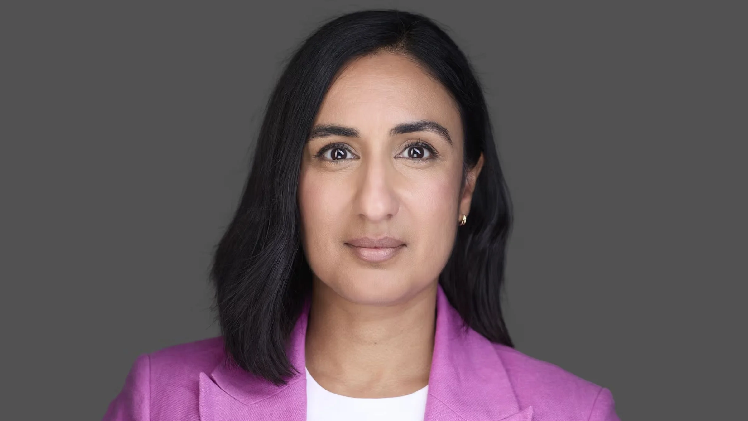 Professional headshot of a woman in a pink blazer against a gray background