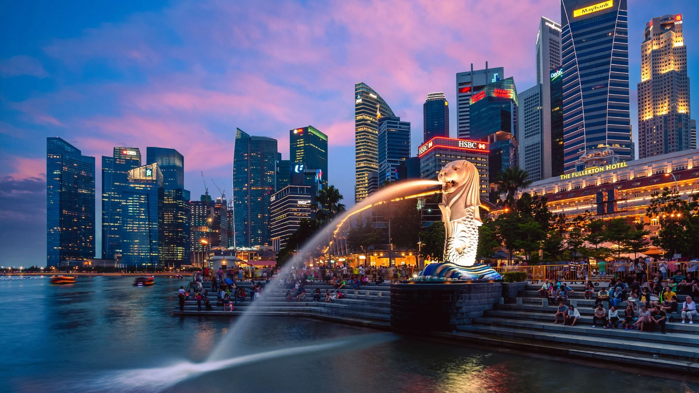 Singapore skyline at dusk with the Merlion fountain and illuminated waterfront buildings along Marina Bay.