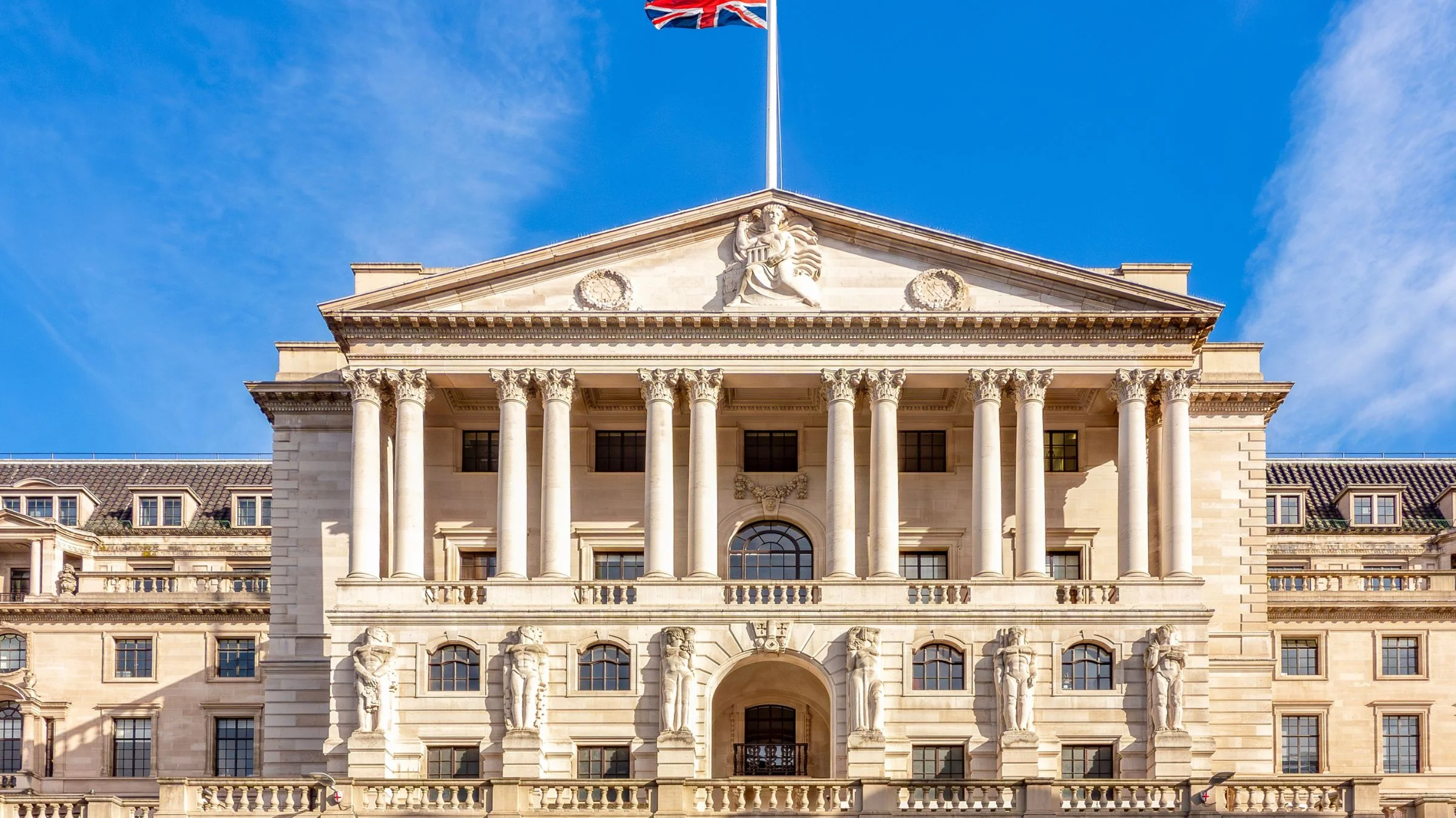 Union Jack flying above a grand neoclassical building with columns under a bright blue sky.