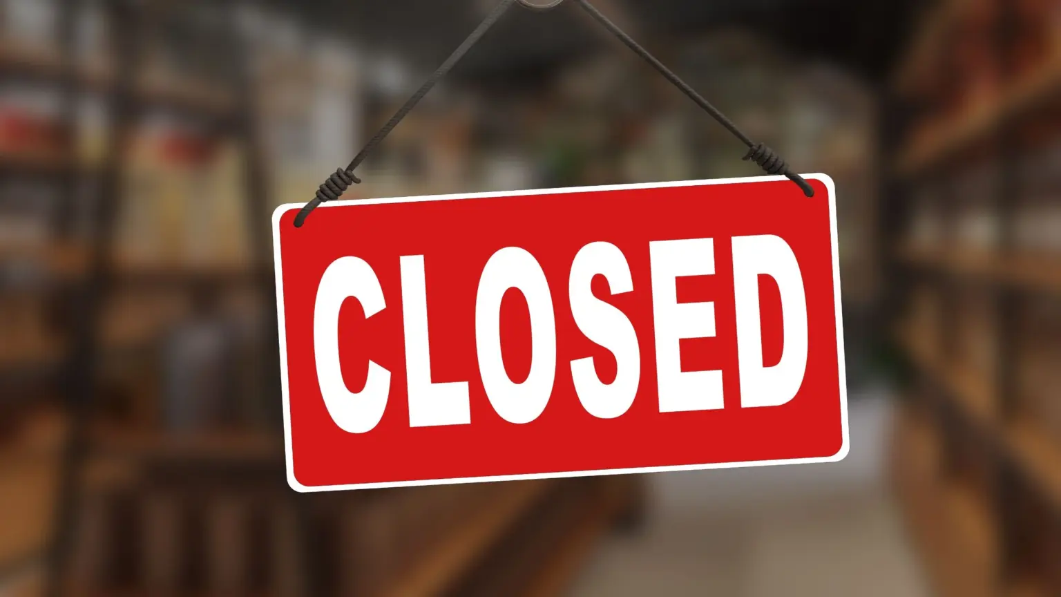 Red closed sign hanging by a rope against a blurred shop or café interior.