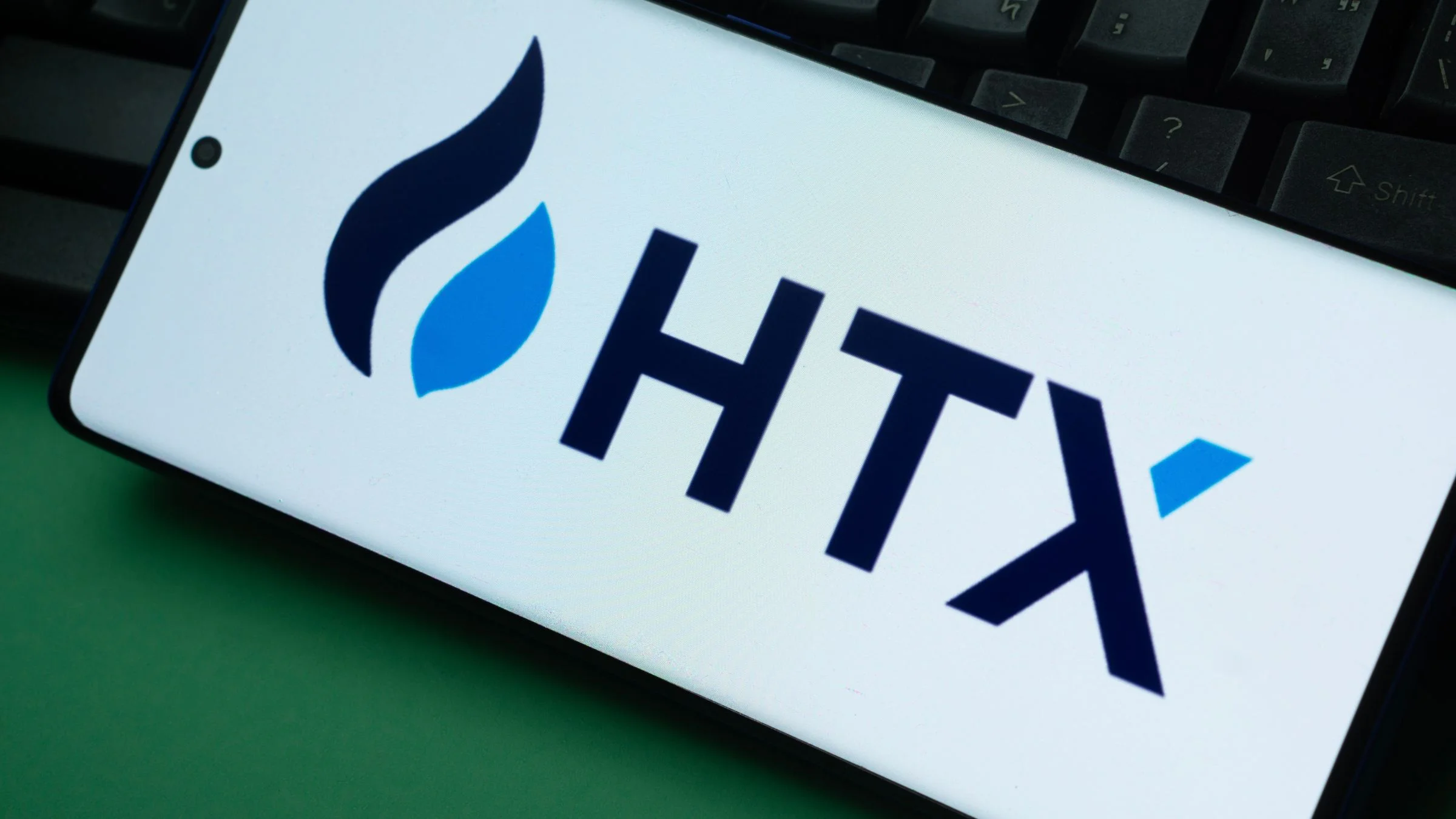 Smartphone displaying the HTX logo placed on top of a computer keyboard in a close-up view.
