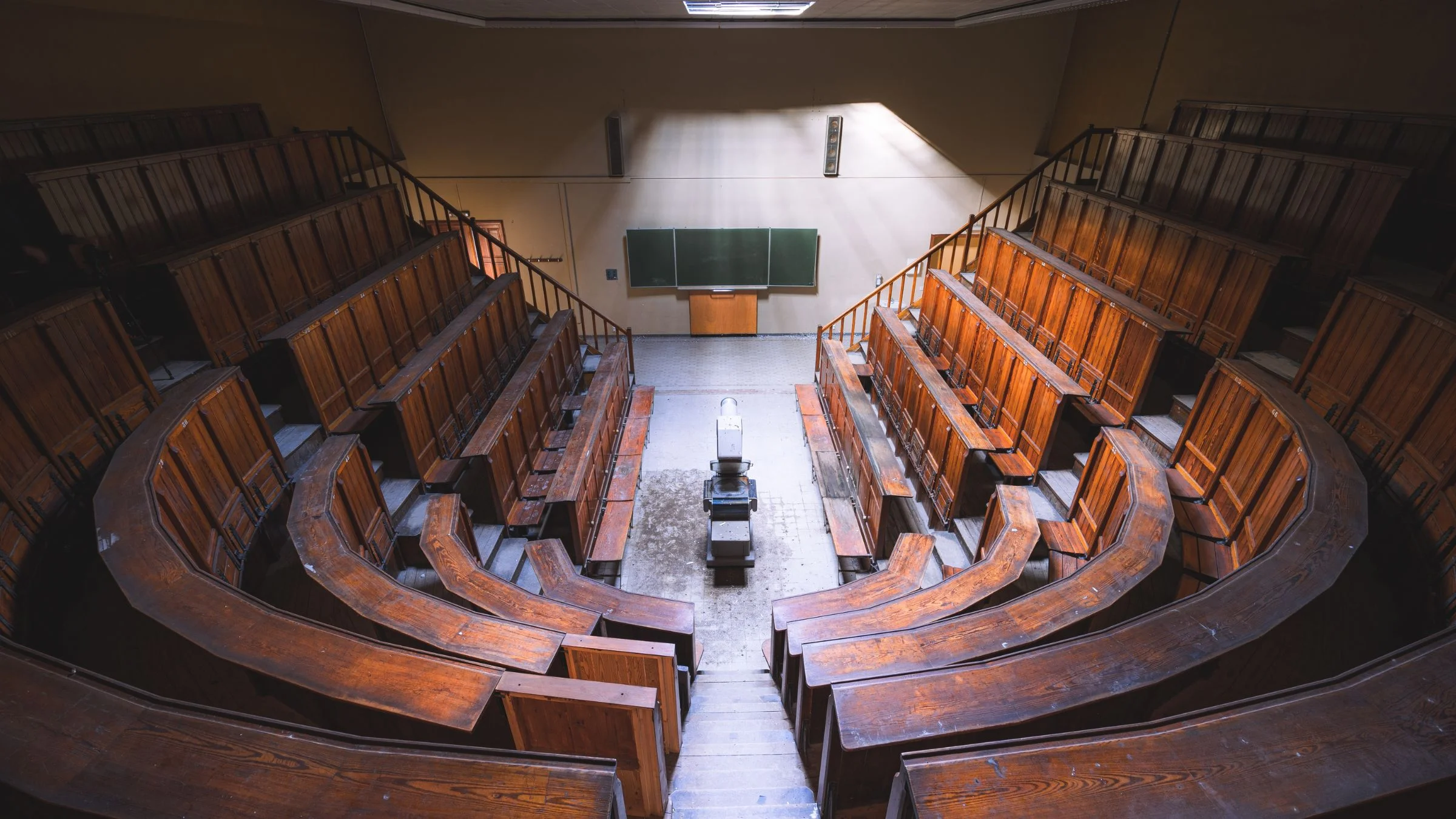 Empty university lecture hall with tiered wooden seating rows and a green chalkboard at the front