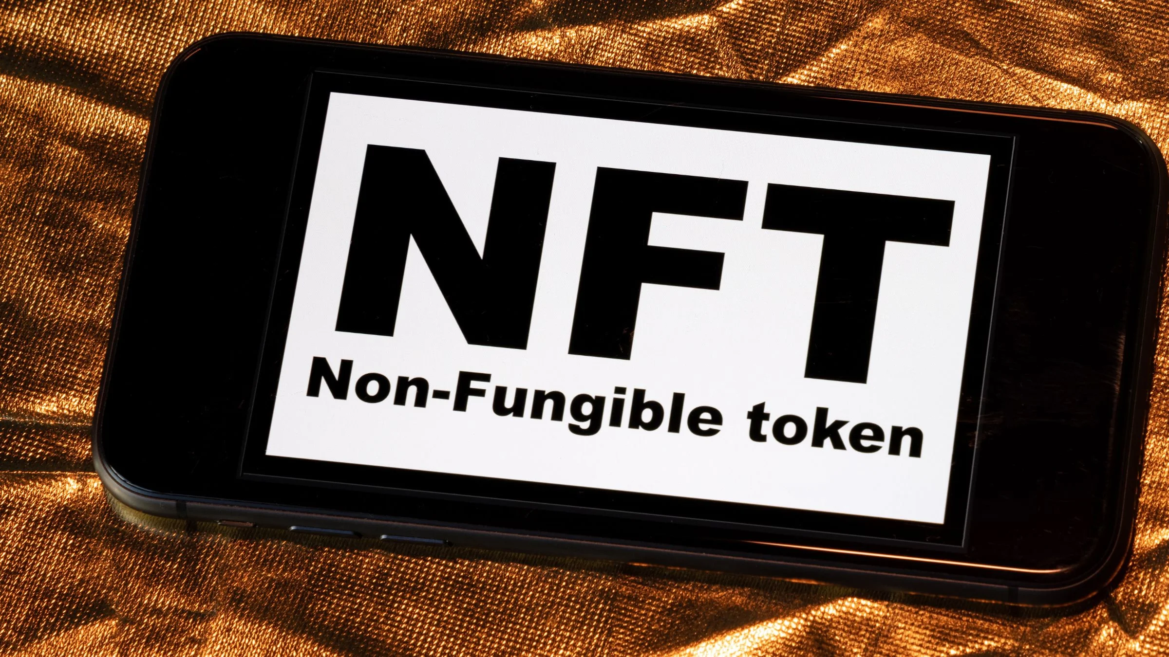 Smartphone screen displaying “NFT” and “Non-Fungible token” text on a gold metallic background.