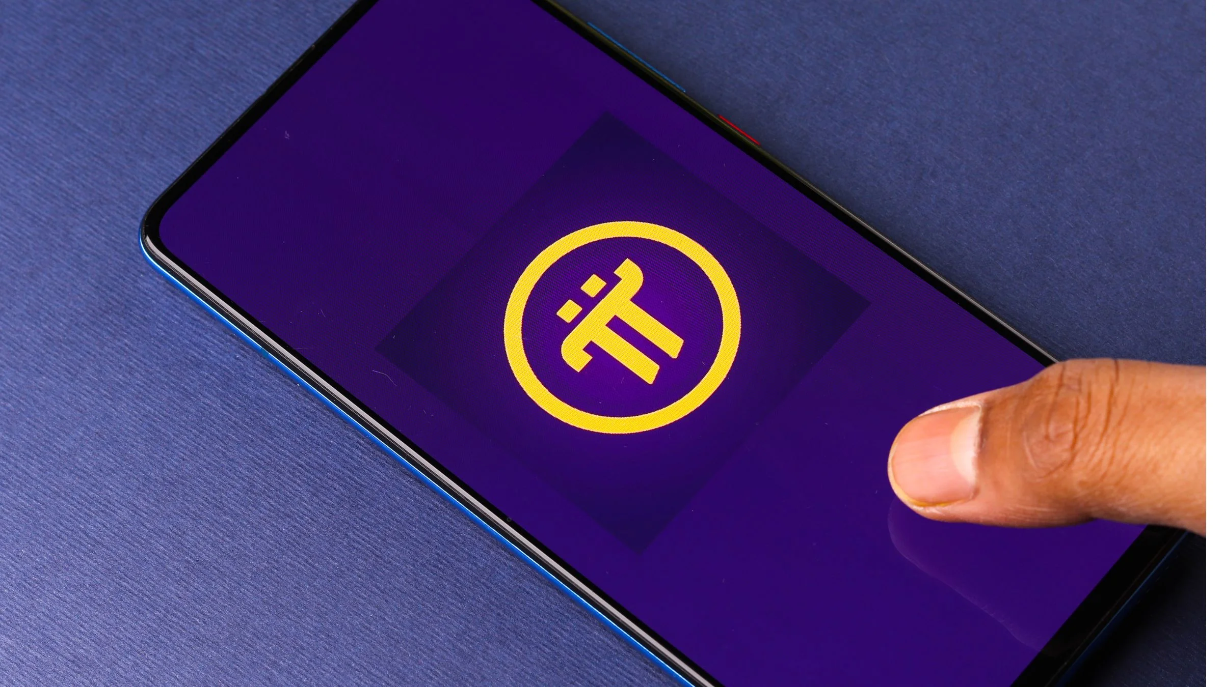 Finger touching a smartphone screen displaying the Pi Network logo on a purple background.