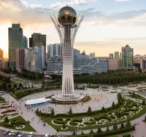 Bayterek Tower rising above central Astana with surrounding government and office buildings at sunset.