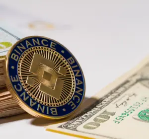 Binance token standing beside stacked U.S. dollar bills and a visible hundred-dollar note
