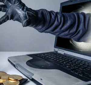 Gloved hand reaching from a laptop toward an open wallet holding Bitcoin coins.