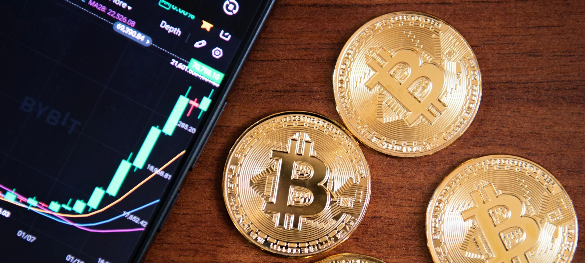 Gold Bitcoin coins beside a phone showing a Bybit price chart