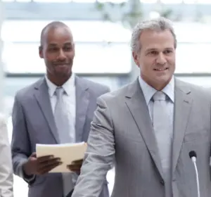 Business executive speaking at a microphone with colleagues standing behind him