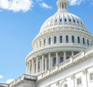 US Capitol dome viewed from below against a blue sky with an American flag