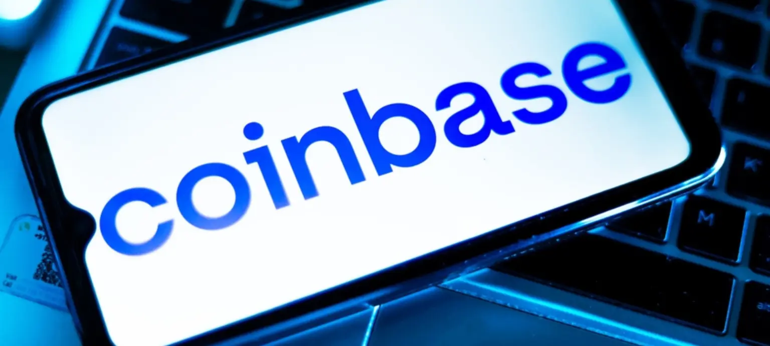 Coinbase logo displayed on a smartphone screen resting on a laptop keyboard