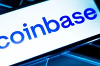 Coinbase logo displayed on a smartphone screen resting on a laptop keyboard