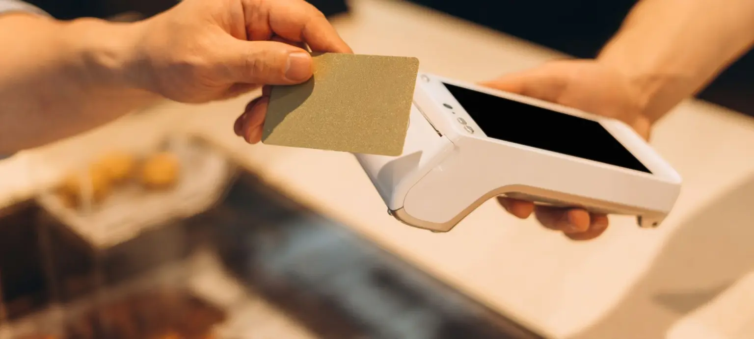 Customer holding a payment card near a handheld point-of-sale terminal during a contactless transaction.