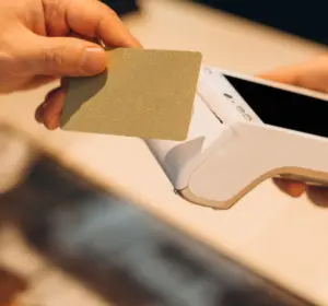 Customer holding a payment card near a handheld point-of-sale terminal during a contactless transaction.