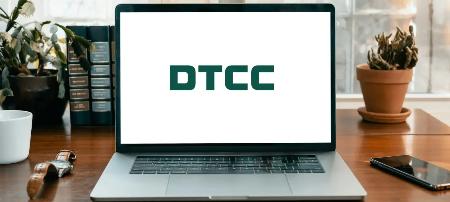 DTCC logo displayed on a laptop screen on a wooden desk with books, plants, and a watch nearby