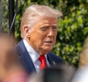 Donald Trump speaks to reporters outdoors while members of the media hold up smartphones and cameras in the foreground.