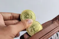 Hand placing two gold Bitcoin tokens into an open brown leather wallet.