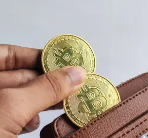 Hand placing two gold Bitcoin tokens into an open brown leather wallet.