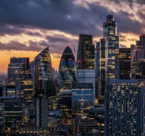 London skyline at sunset with illuminated skyscrapers including the Gherkin and the Shard beneath dramatic clouds