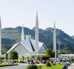 Faisal Mosque in Islamabad with four minarets and green Margalla Hills in the background.